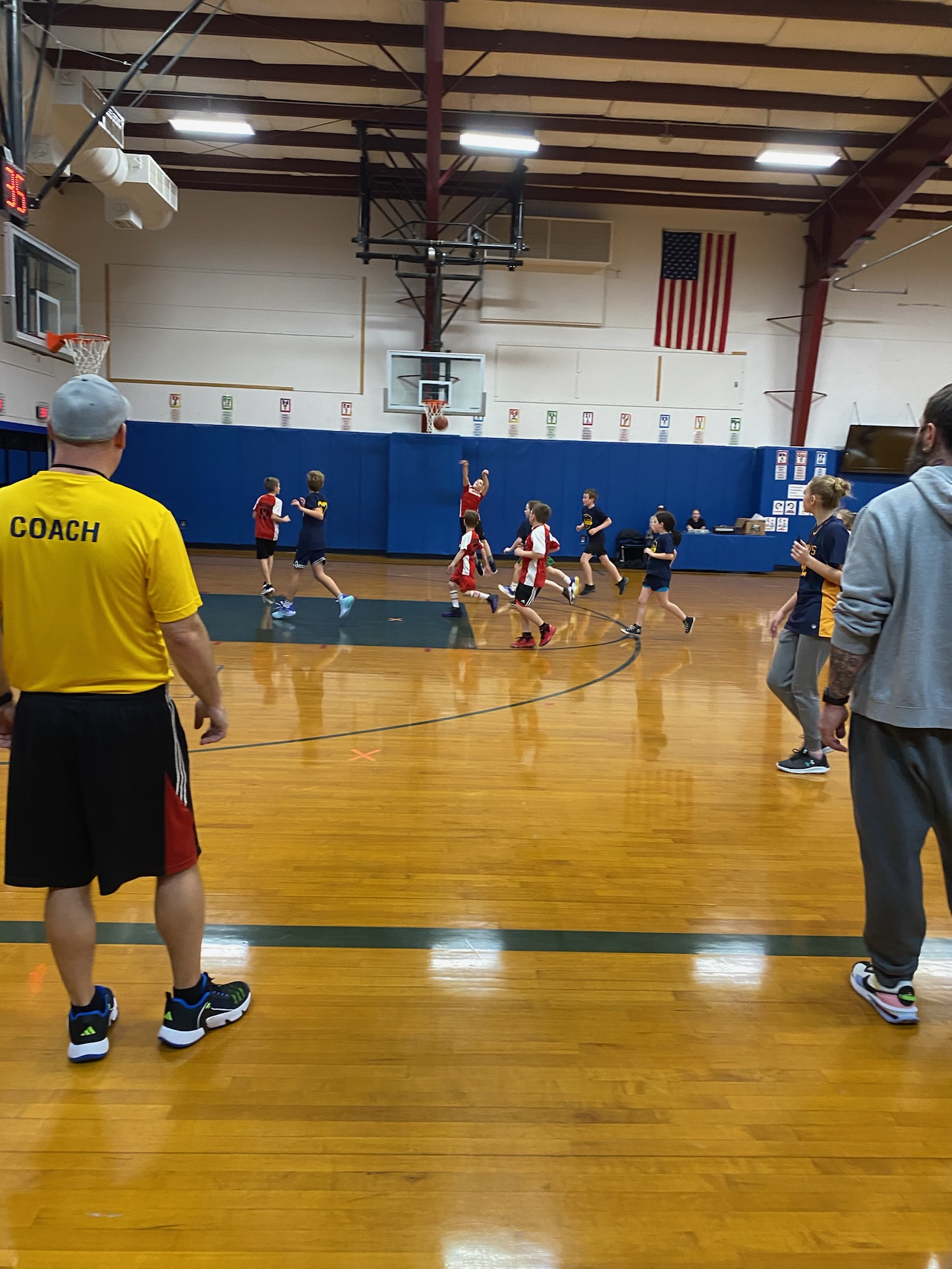 kids playing basketball in a gymnasium with their coaches watching