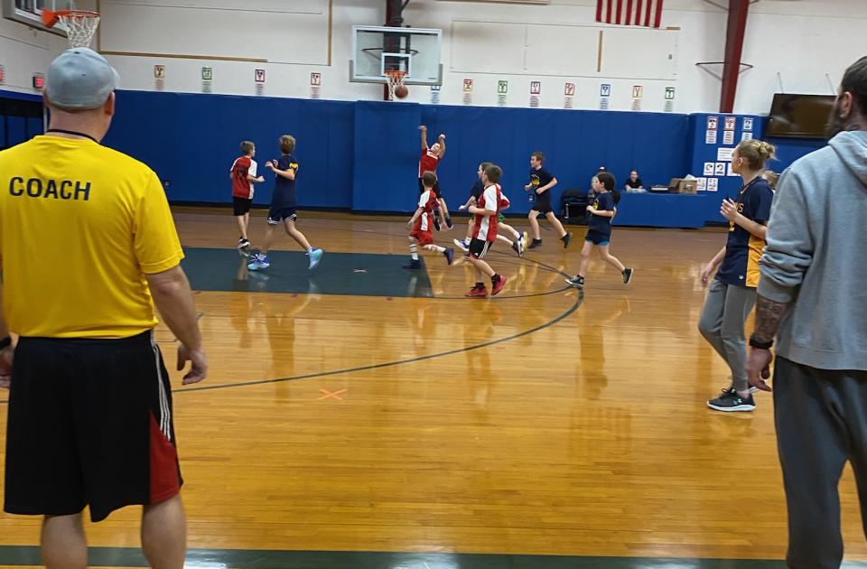 kids playing basketball in a gymnasium with their coaches watching